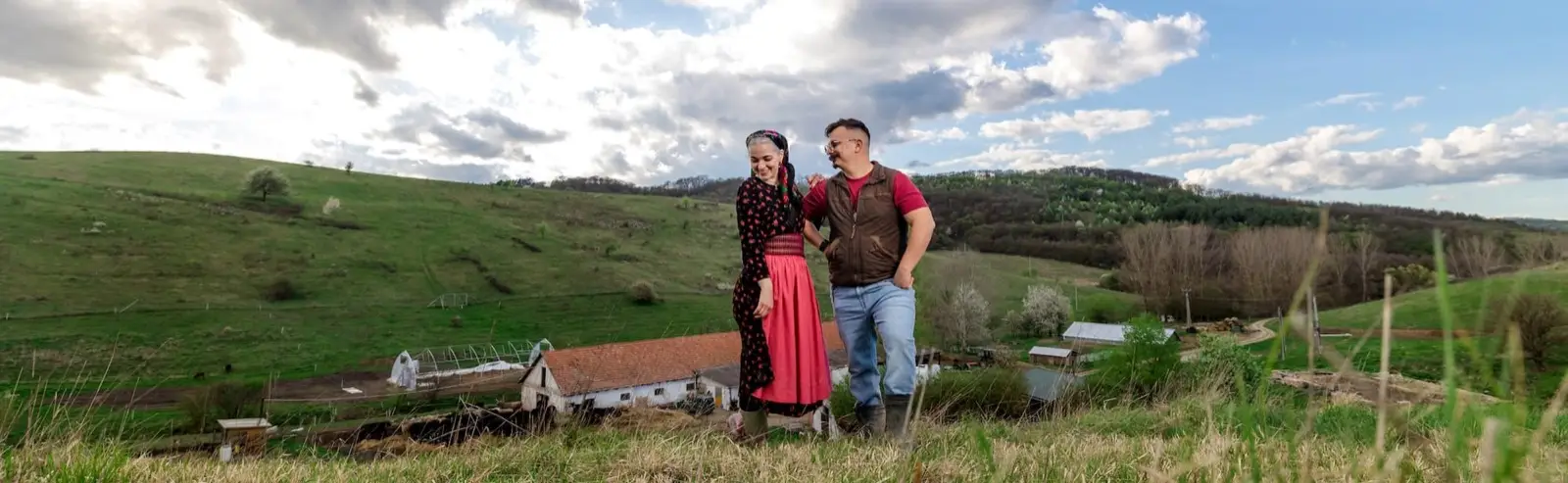 Népviseletbe öltözött pár áll egymás mellett a farm feletti dombon